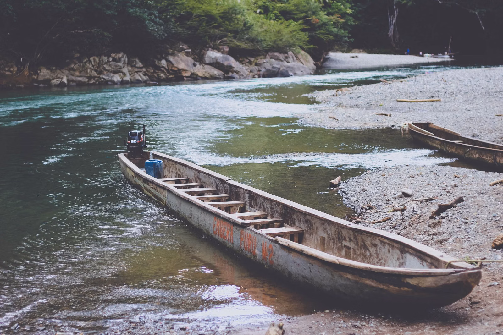 A long wooden canoe pulled up on the gravel bank of a clear creek