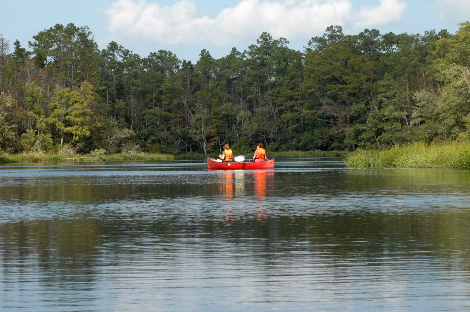 Two people paddling a red canoe on a calm, tree-lined river
